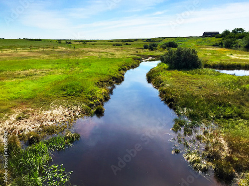 Rural prairie landscape with a boggy creek running through marsh land in summer.