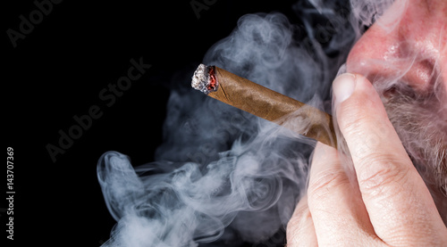 A man smokes a cigar against black background 