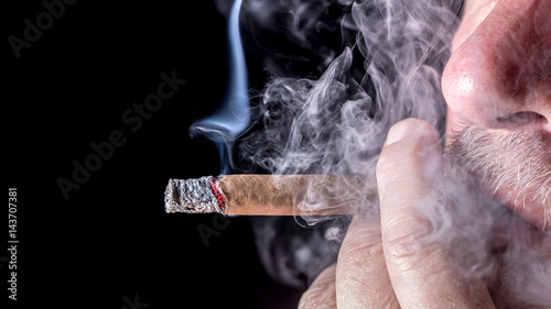 A man smokes a cigar against black background 