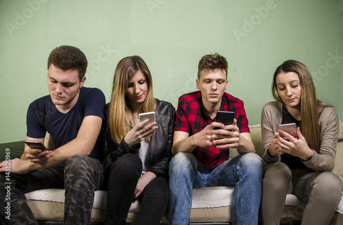 Young people sitting on couch indoors preoccupied with smartphones 