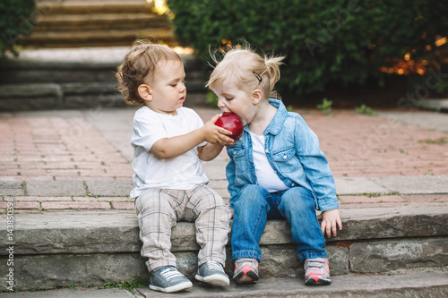 Group portrait of two white Caucasian cute adorable funny children toddlers sitting together sharing eating apple food, love friendship childhood concept, best friends forever