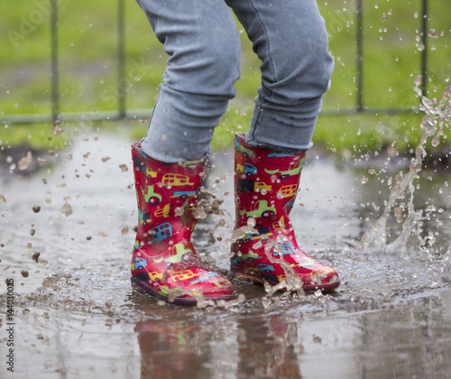 dziecko w kaloszach bawiące się w deszczu