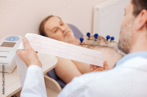 Excellent trained cardiologist carefully studying patients cardiogram