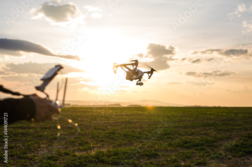 Man operating a drone with remote control. Dark silhouette against colorful sunset.