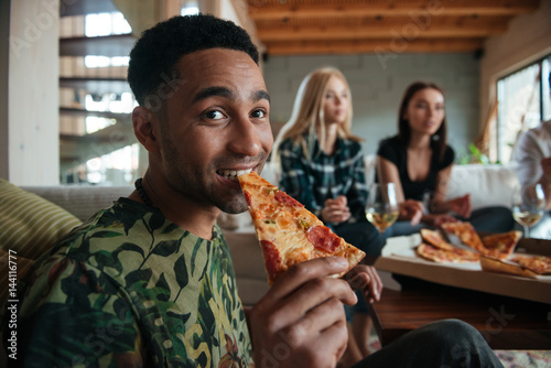 Man eating slice of pizza while hanging out with friends