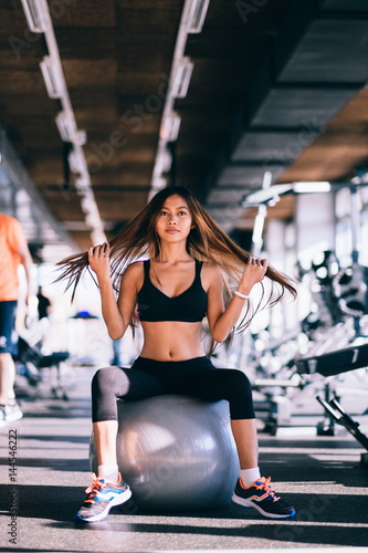 Fitness young woman with long hair in gym, sitting on pilates ball