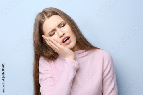 Young woman suffering from toothache on light background