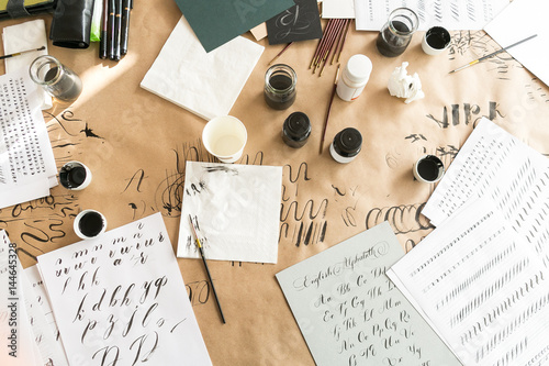 Calligraphy sheets, nibs, paper, ink and pens on a kraft background. Lettering calligraphy workshop. Letters of the English alphabet written with a paint brush. Concept hobby. top view, flat lay.