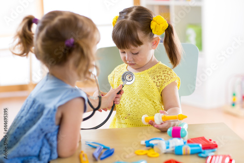 Two cute children playing doctor and hospital using stethoscope. Friends girls having fun at home or preschool.