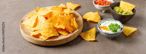 Snack for a party, chips with a tortilla, nachos with sauces: salsa with tomatoes, sour cream and guacamole. Mexican food. Dark background. Copy space