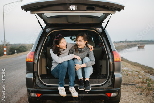 Two happy Asia woman friends enjoying road trip in hatchback car,flare light