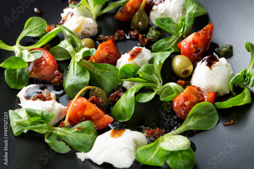 Caprese salad with mozzarella, tomato, basil and balsamic vinegar arranged on black plate. Close up image with selective focus