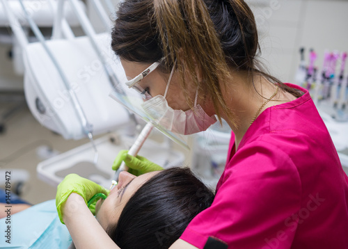 Female dentist cleaning teeth of a beautiful patient woman in dental clinic