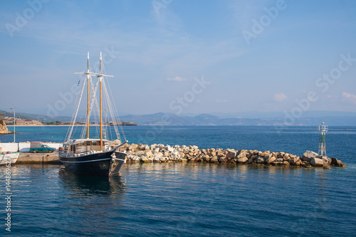 An old frigate moored at the pier. Black medieval wooden ship on the water. The ship in the Ionian sea. Rocky pier.