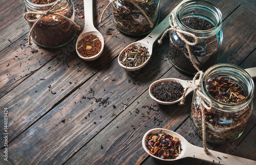 Different kinds of tea in jar and wooden spoons on wood table