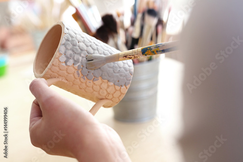 Szkliwienie ceramiki. Kobieta maluje szkliwem gliniany kubek