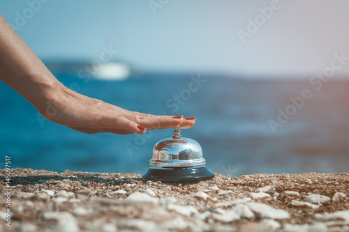 Close up of female hand ringing service bell against the ocean background. Summertime concept.