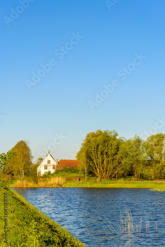 Idyllic place with an old white plastered farmhouse on the banks of a natural pond