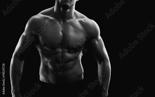 Horizontal cropped black and white studio shot of a muscular sexy torso of an athletic man posing shirtless on black background copyspace fitness strength athletics power sports bodybuilding concept.