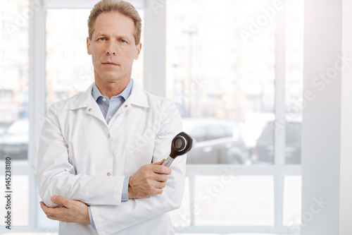 Confident aged dermatologist holding dermatoscope at work