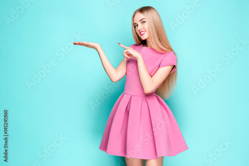 Smiling beautiful young woman in pink mini dress posing, presenting something