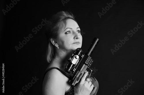 A middle aged, white, woman holds a semi automatic pistol with silencer and collimator against black