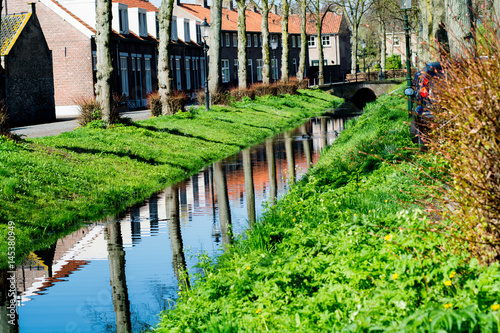 Walking along the small canal in old Dutch village, sunny Sunday morning, reflection in water.