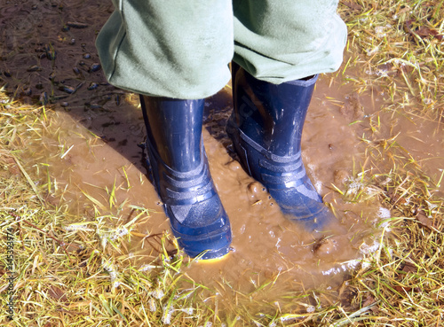 Closeup of boy in blue rain boots splashing in a muddy puddle after the rain