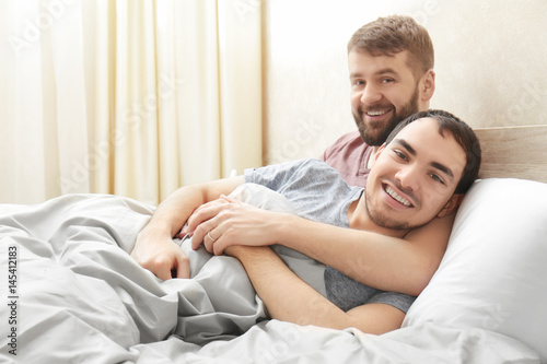 Happy gay couple hugging in bed at home