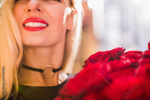 Close-up half face of woman near red roses, outdoors