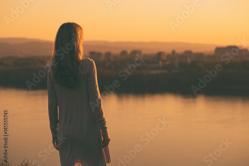 Lonely woman standing and looking at the sunset over the city.