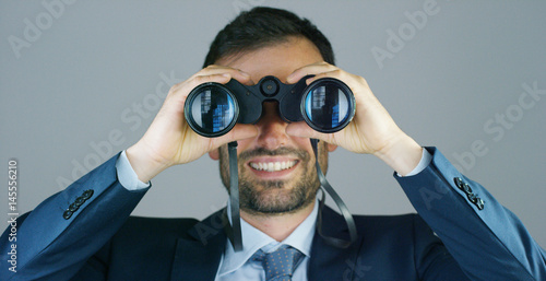 A businessman in a suit and tie, use the binoculars to look away with the concept of looking to the future, forecasting the economic and financial growth and the future