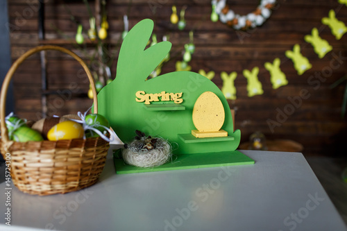 Easter background. Colored eggs in a basket on dark wooden background with a wooden green rabbit
