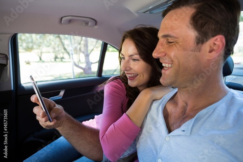 Happy couple using mobile phone in car
