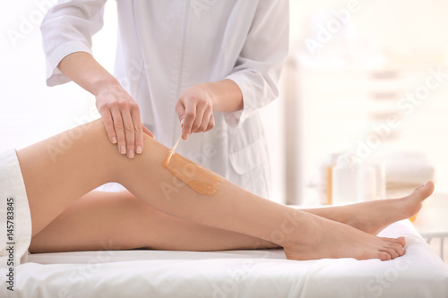 Beautician waxing female legs in spa center