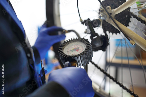 Pompowanie koła rowerowego. Mechanik w serwisie rowerowym pompuje koło roweru kompresorem ze sprężonym powietrzem.