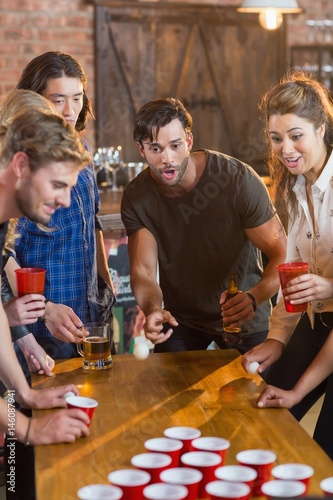 Friends looking at ball while man playing beer pong in bar