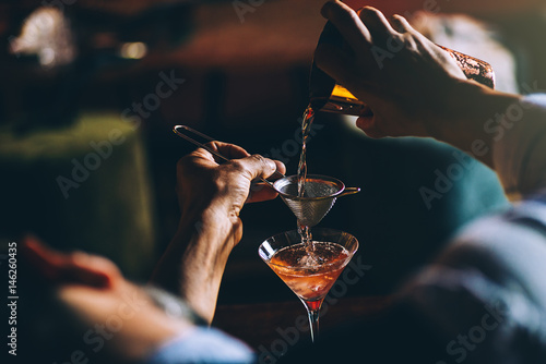 Barman is making cocktail at night club.