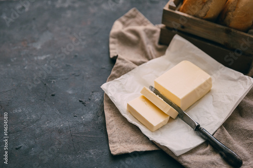 Pat of fresh farm butter with a knife and bread over rustic background