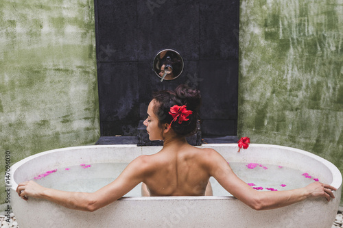 Woman relaxing in round outdoor bath with tropical flowers, organic skin care, luxury spa hotel, lifestyle photo