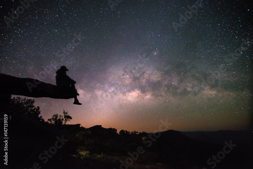 Woman sits on stone lodge and look night sky stars with milky way background