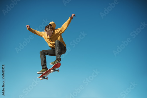 A teenager skateboarder does an ollie trick on background of blue sky gradient