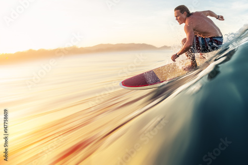 Surfer rides the perfect ocean wave at sunrise. Motion blurred water