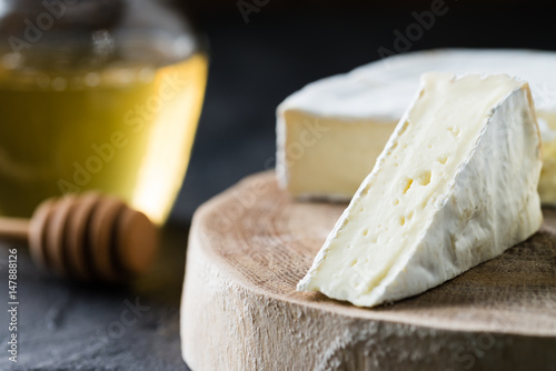 Closeup of soft cheese brie sliced on wooden cut with honey and spoon on dark rustic background
