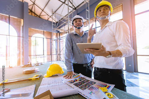 customer and constructor foreman worker with helmet and vest looking blueprints in new house building in real state business and housing industry concept. data in touch pad