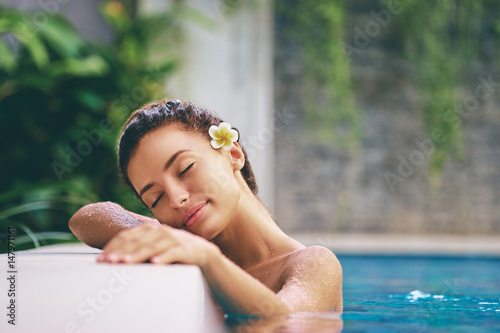 Pielęgnacja urody i ciała. Zmysłowa młoda kobieta relaksuje w plenerowym zdroju pływackim basenie.