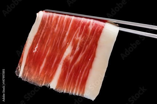 Piece of cured ham on tweezers.