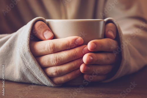 Man's hands holding a mug and warming with hot tea in the evening.