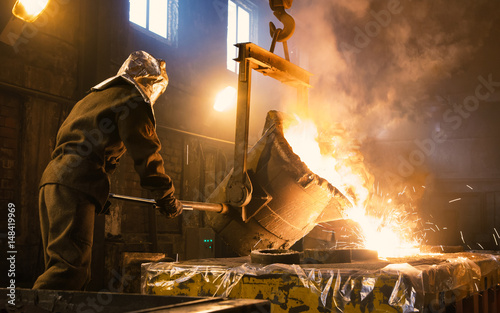 Worker controlling metal melting in furnaces. Workers operates at the metallurgical plant. The liquid metal is poured into molds.