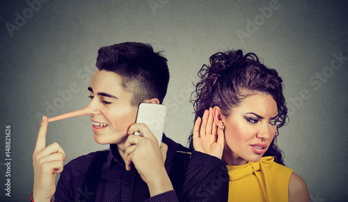 Curious worried woman secretly listening to a happy man liar talking on mobile phone with his lover